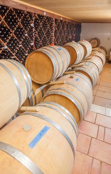 Wine Barrels and Bottles Age Inside Dark Cellar.