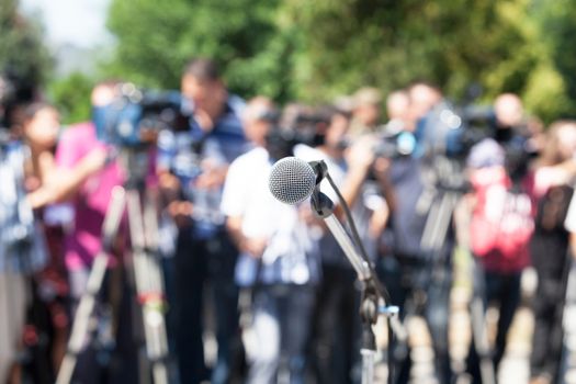 News conference. Microphone in focus against blurred camera operators and reporters.