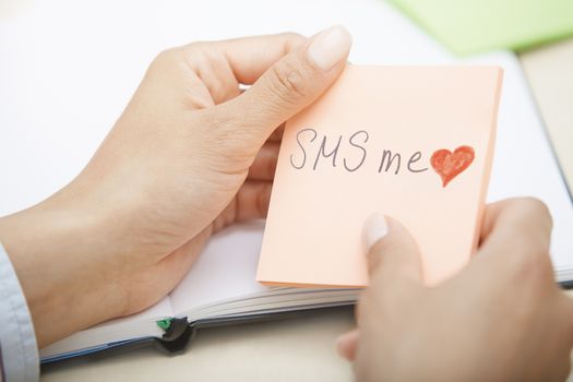Hands holding sticky note with SMS me text