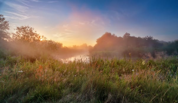 Summer misty sunrise on the river. Foggy river in the morning. Misty morning panorama.