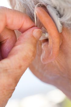 closeup senior woman inserting hearing aid in her ears