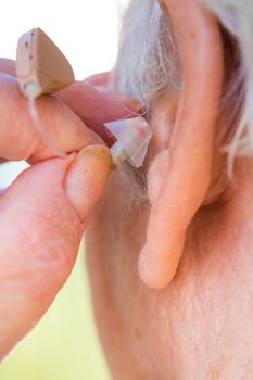 closeup senior woman inserting hearing aid in her ears