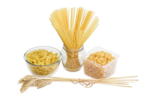 Uncooked dried long pasta in glass jar, macaroni in glass bowl, pasta seashell shaped  in plastic tray and bundle of wheat spikes on a light background
