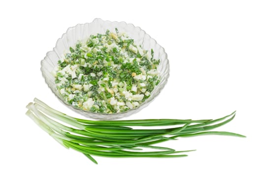 Spring salad with chopped green onions, boiled eggs and sour cream in a glass salad bowl and a bunch of green onions on a light background
