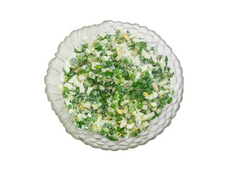 Top view to a spring salad with chopped green onions, boiled eggs and sour cream in a glass salad bowl on a light background
