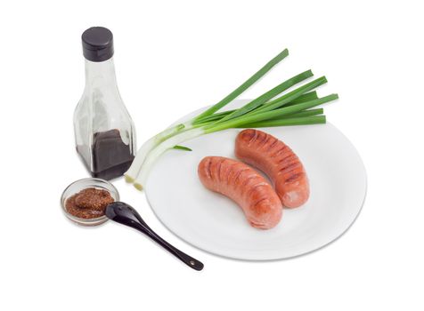 Two fried thick frankfurters and green onion on a white dish, coarse French mustard and soy sauce on a light background
