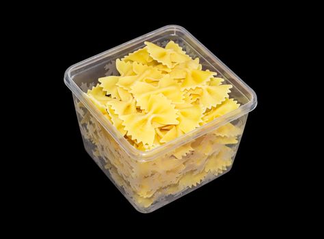 Uncooked bow-tie pasta in transparent plastic tray on a dark background
