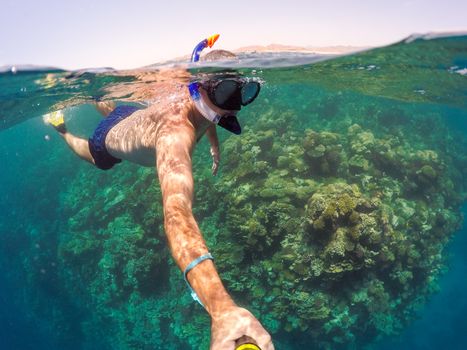 Underwater and surface split view in the tropics paradise with snorkeling man, fish and coral reef, under and above waterline, beautiful view on tropical sea. Egypt. Holiday snorkeling vacation concept