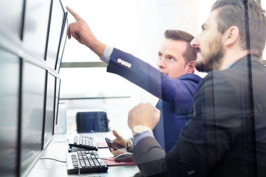 Businessmen trading stocks. Stock traders looking at graphs, indexes and numbers on multiple computer screens. Colleagues in discussion in traders office. 