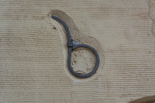 Rusty antique wall anchor in an old yellow painted and plastered stone wall.