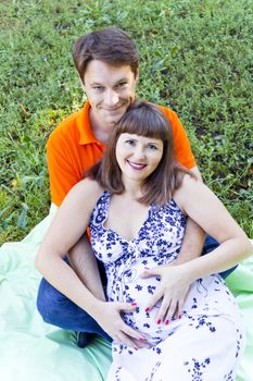 Husband and pregnant wife sitting on green grass in summer time