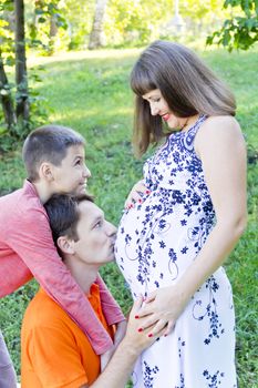 Happy family husband kissing pregnant wife stomach in summer time