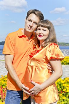 Husband embraces pregnant wife in summer embankment