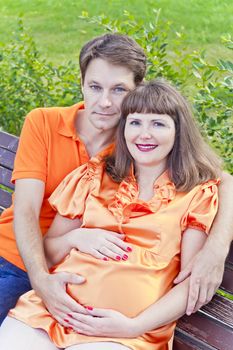 Husband and pregnant wife sitting on bench in summer time