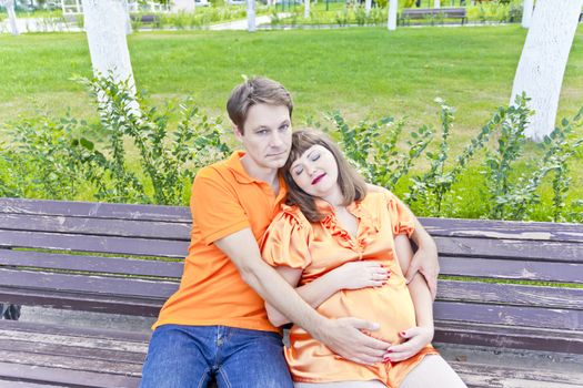 Husband and pregnant wife sitting on bench in summer time