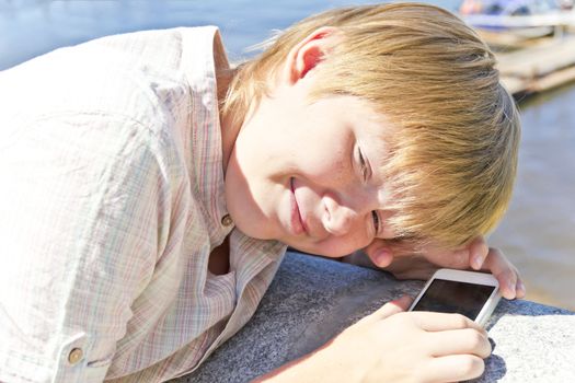 Blonde smiling boy with cellular phone in sunlight