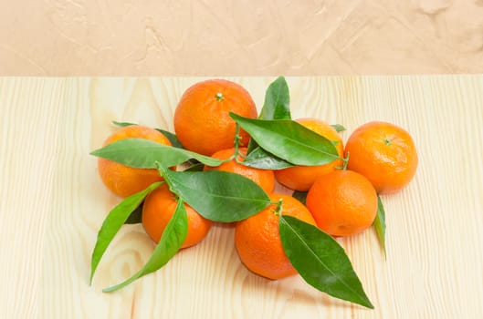Several fresh ripe mandarin oranges with branches and leaves on a light wooden surface

