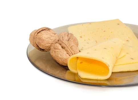 Several slices of a semi-hard cheese made with pounded walnuts and several whole walnuts on a glass dish on a light background
