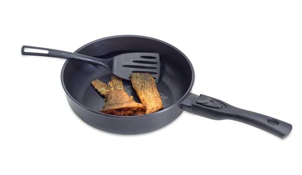 Fried tail portion and other slice of carp and plastic spatula on an aluminium cast frying pan with ceramic non-stick coating on a light background
