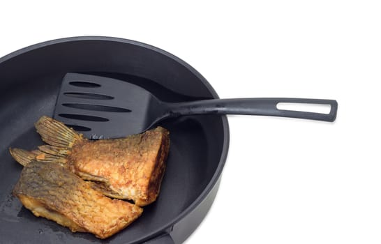 Fragment of an aluminium cast frying pan with ceramic non-stick coating with fried tail portion and other slice of carp and plastic spatula on a light background
