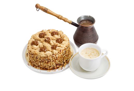 Round sponge cake, decorated with butter cream and caramelized condensed milk, sprinkled with grated nuts, old copper coffee pot and coffee with cream in white cup on a light background
