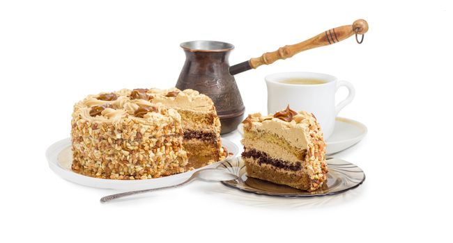 Partly sliced layered sponge cake, decorated with butter cream, caramelized condensed milk and nuts on background of coffee cup and old coffee pot on a light background
