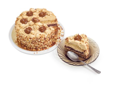 Piece of layered sponge cake, decorated with butter cream, caramelized condensed milk and nuts with spoon on a glass saucer and partly sliced cake on a light background
