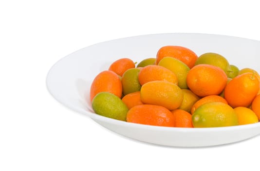 Fragment of white dish with fresh oval kumquats closeup on a light background
