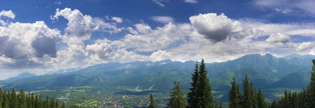 Summer panorama of massif with mountain ranges and town in the valley on the background of the sky with clouds in the Tatra Mountains 
