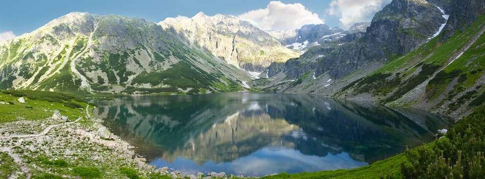 Panorama of a mountain lake on the background of the craggy mountain slopes
