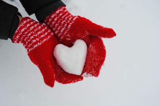 woman in red mittens holding a snowy heart.