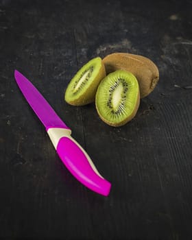 Kiwi fruit and a colored knife over a dark wooden table,
