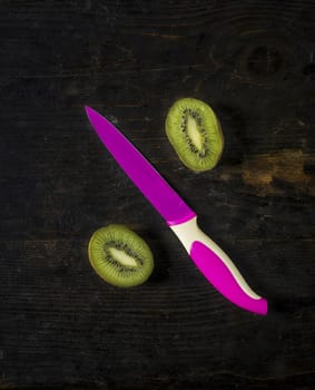 Kiwi fruit and a colored knife over a dark wooden table,