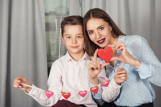 Happy Valentines Day or Mother day. Young boy spend time with her mum and celebrate with gingerbread heart cookies on a stick.