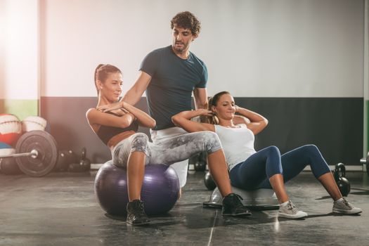 Two girl exercising at the gym with a personal trainer.