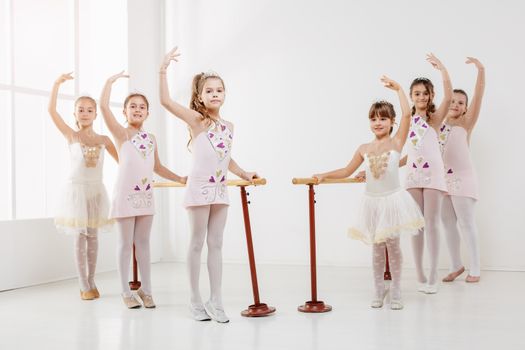 Little girls using barre while practicing in dance studio. Looking at camera.