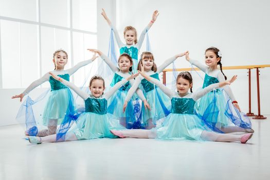 Smiling little girls in dresses practicing postures during ballet class. Looking at camera.
