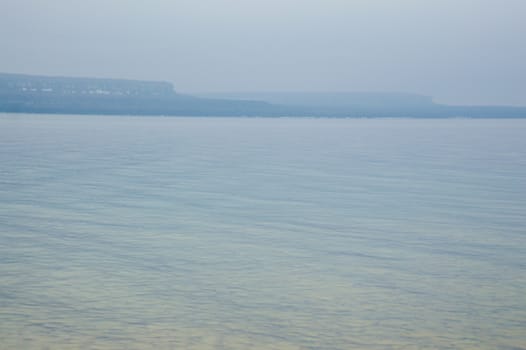 Image has the limestone escarpment cliffs in the distance with reflected yellow and blue ripples and waves in the crystal clear lake