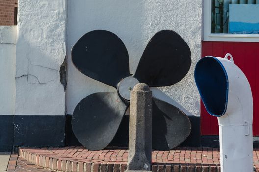 Ship equipment in front of a building wall. Large ship's screw and ventilation shaft.