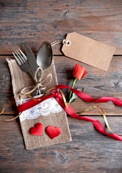 Valentines day label attached to cutlery inside a pouch with decorative ribbon and a single rose