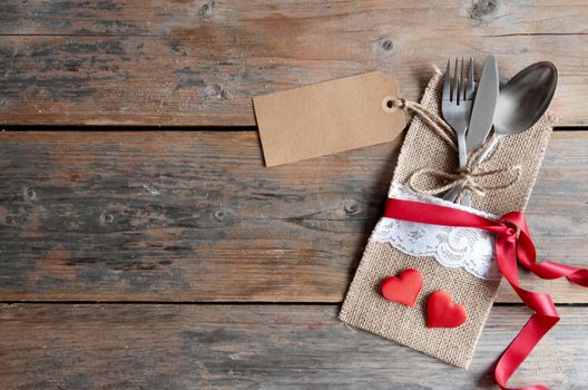 Empty label attached to cutlery inside a pouch with decorative ribbon over a wooden background