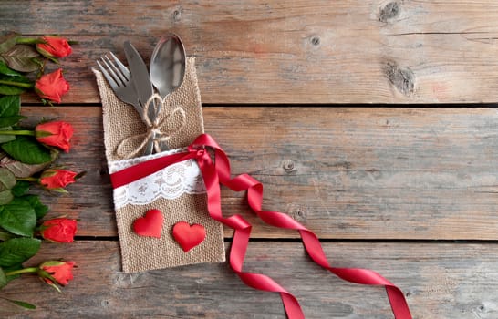 Valentines day cutlery set inside pouch with red roses and hearts over a wooden background