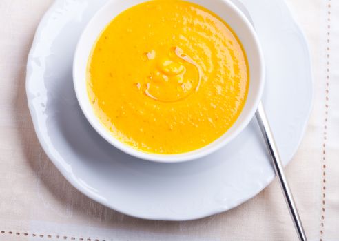 Pumpkin creme soup with a spoon on a white background