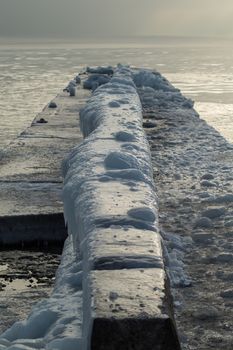 ice-covered pier on the seashore. Frosty winter dawn. Huge icicles on a pier