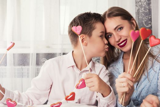 Happy Valentines Day or Mother day. Young boy spend time with her mum and celebrate with gingerbread heart cookies on a stick.