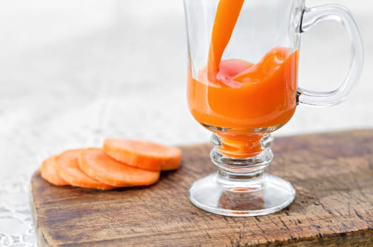 Carrot juice is poured into a glass Cup on a stem which stands on the table and the chopping Board, close can't see the edge. Selective focus and place for text.