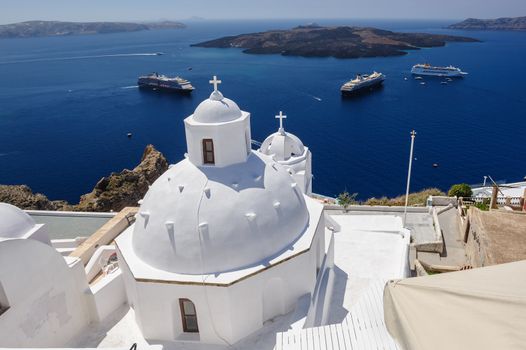 White orthodox church bell tower and sea with ships at background. Fira, Santorini Greece. Copyspace