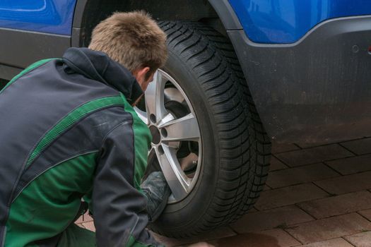 Young man  exchanging the car tires. From summer tires on winter tires on his car.