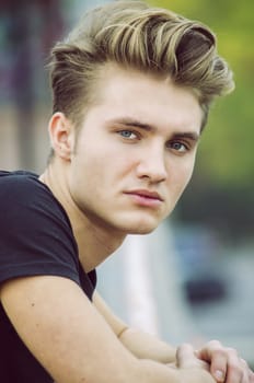 Profile shot of attractive blond young man in city, looking at camera, outdoor