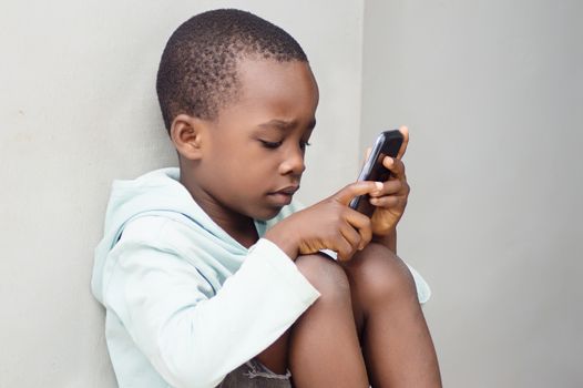a child sitting against the wall manipulating a mobile phone with curiosity.